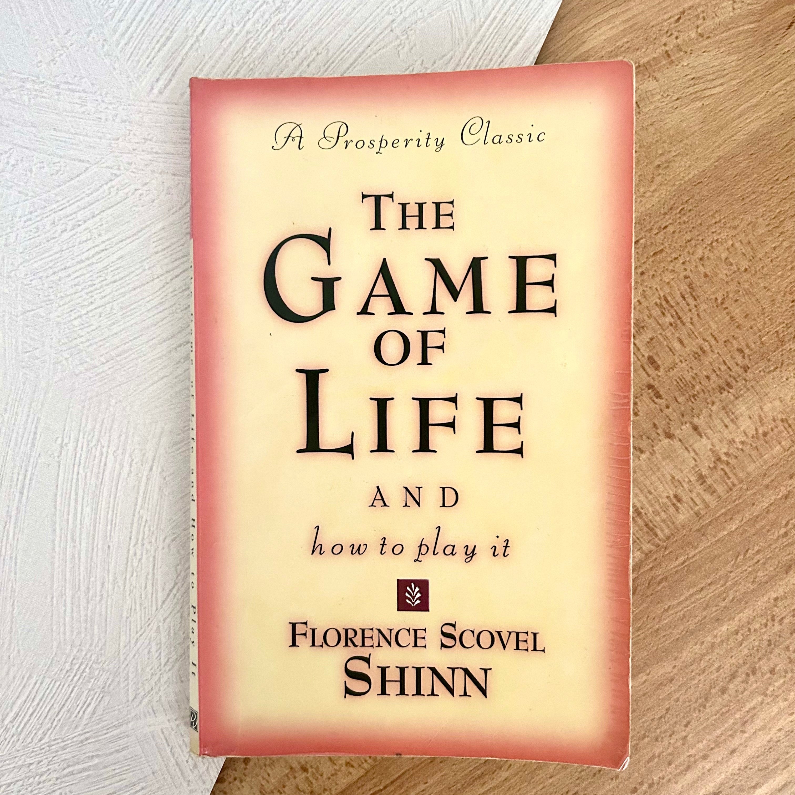 Paperback book of The Game of Life and How to Play It on white and wooden background