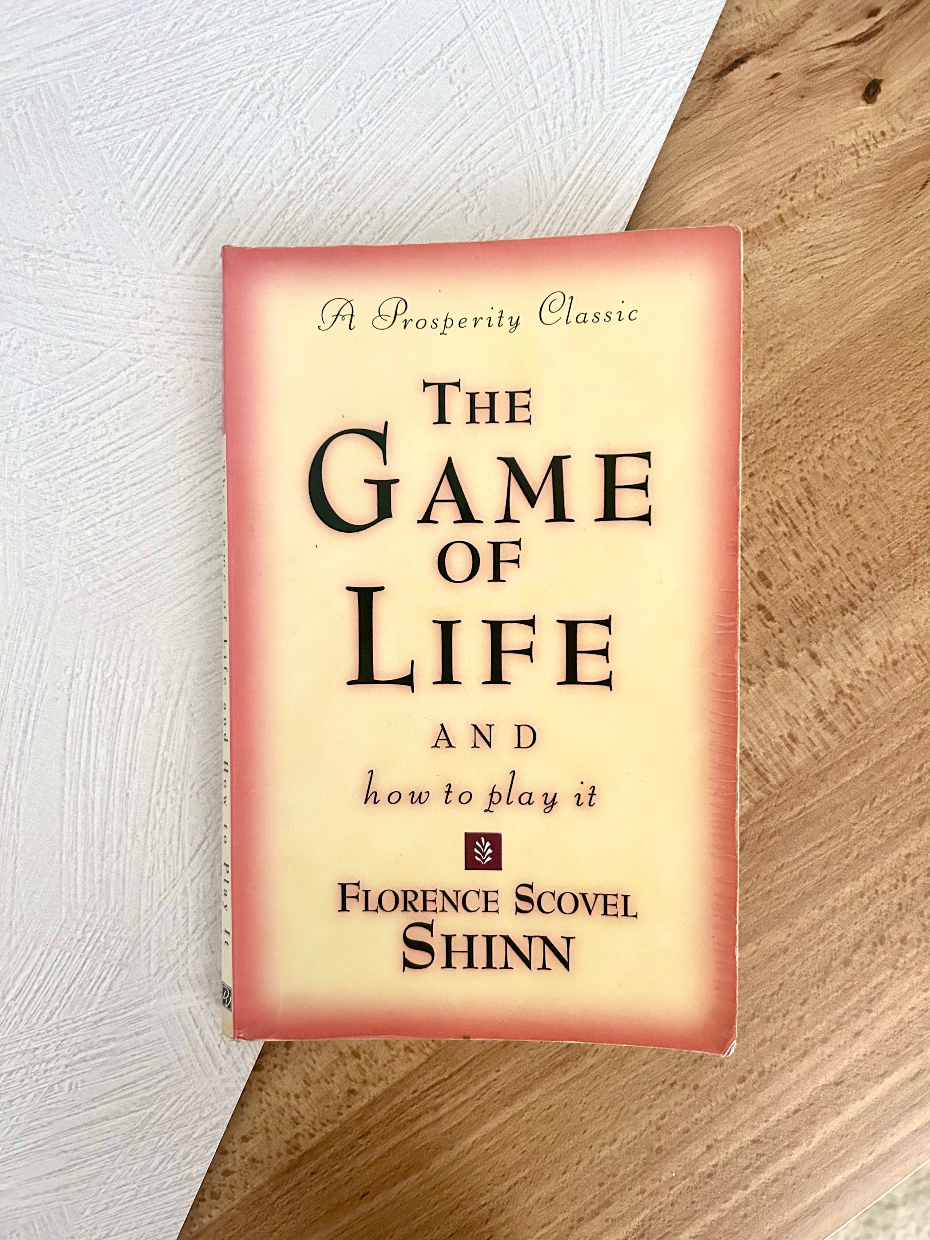 Paperback book of The Game of Life and How to Play It on white and wooden background