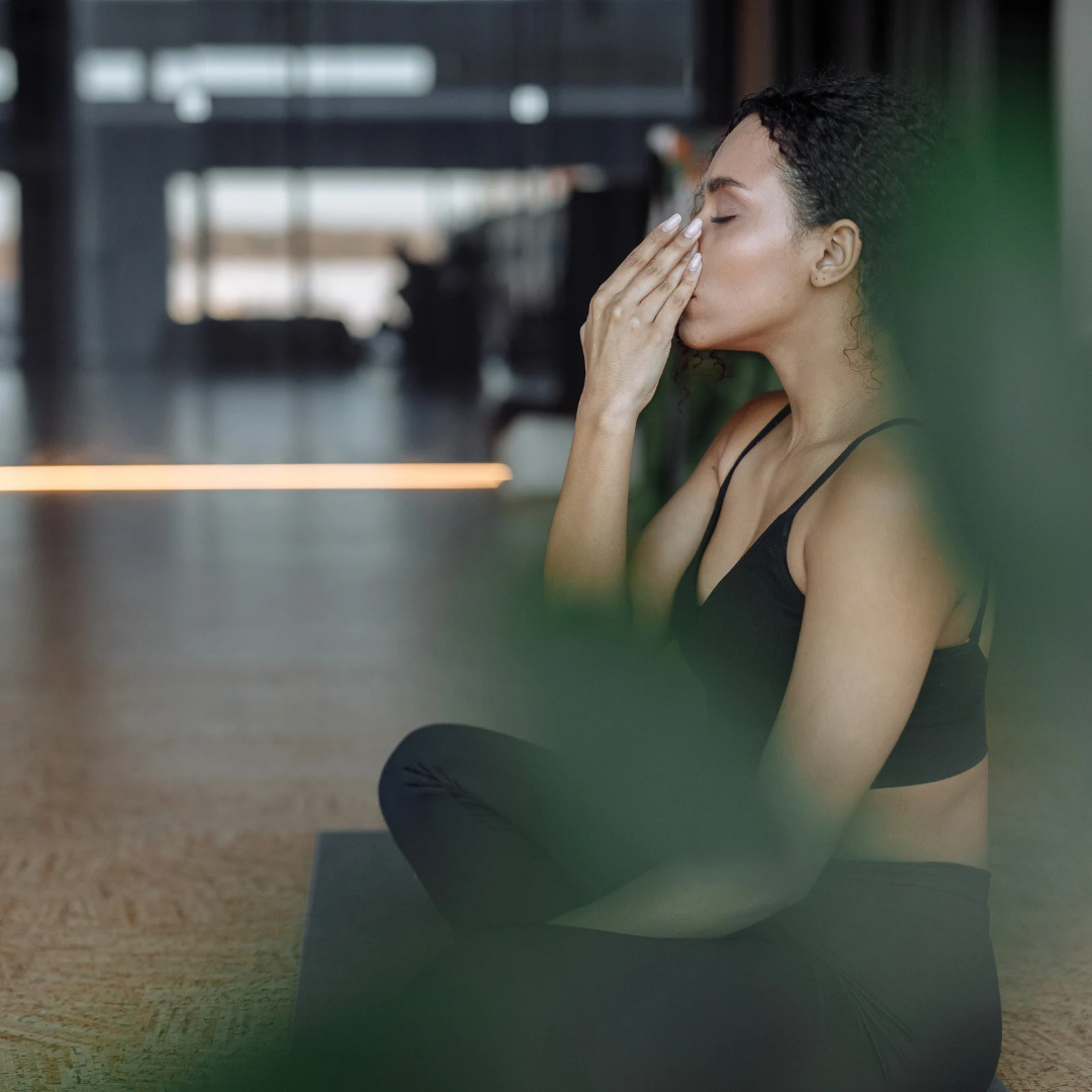 Woman with Natural Curly Hair in Black Active Wear Concentrating while Sitting on a Yoga Mat for Health and Wellness.